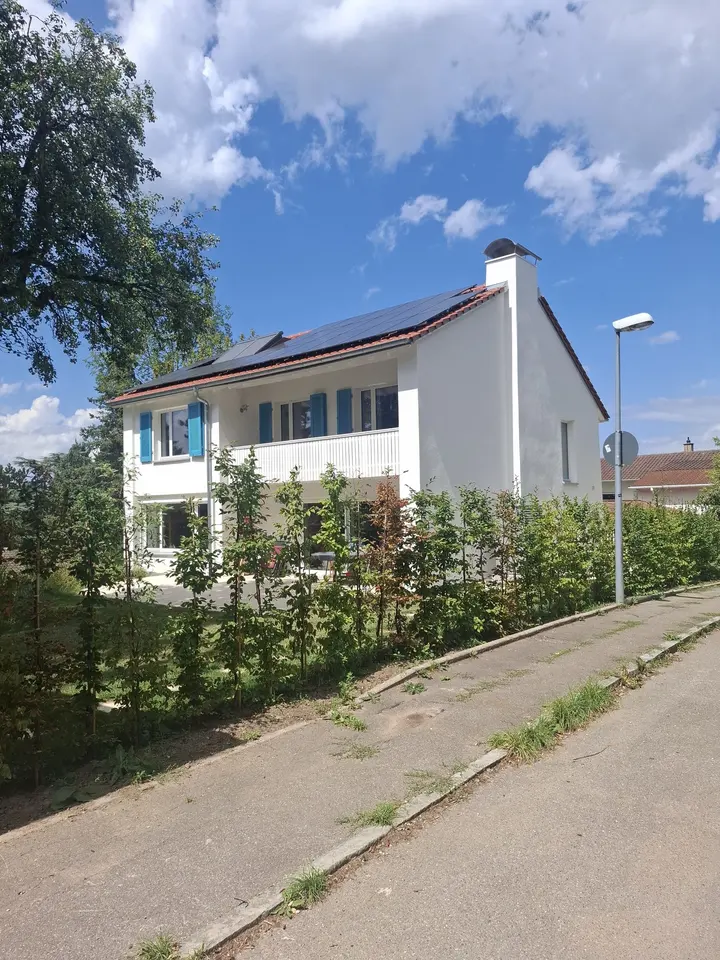 Fertig verputztes Wohnhaus mit weißer Fassade, blauen Fensterläden und Photovoltaikanlage