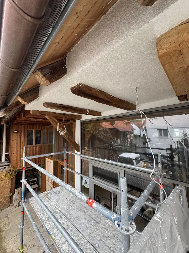 Frisch verputzte Dachuntersicht zwischen freigelegten Holzbalken, davor ein Arbeitsgerüst
