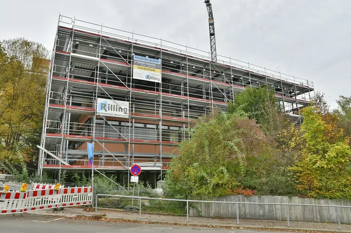 Eingerüstetes mehrgeschossiges Gebäude mit Werbeplane von Rilling und Baukran