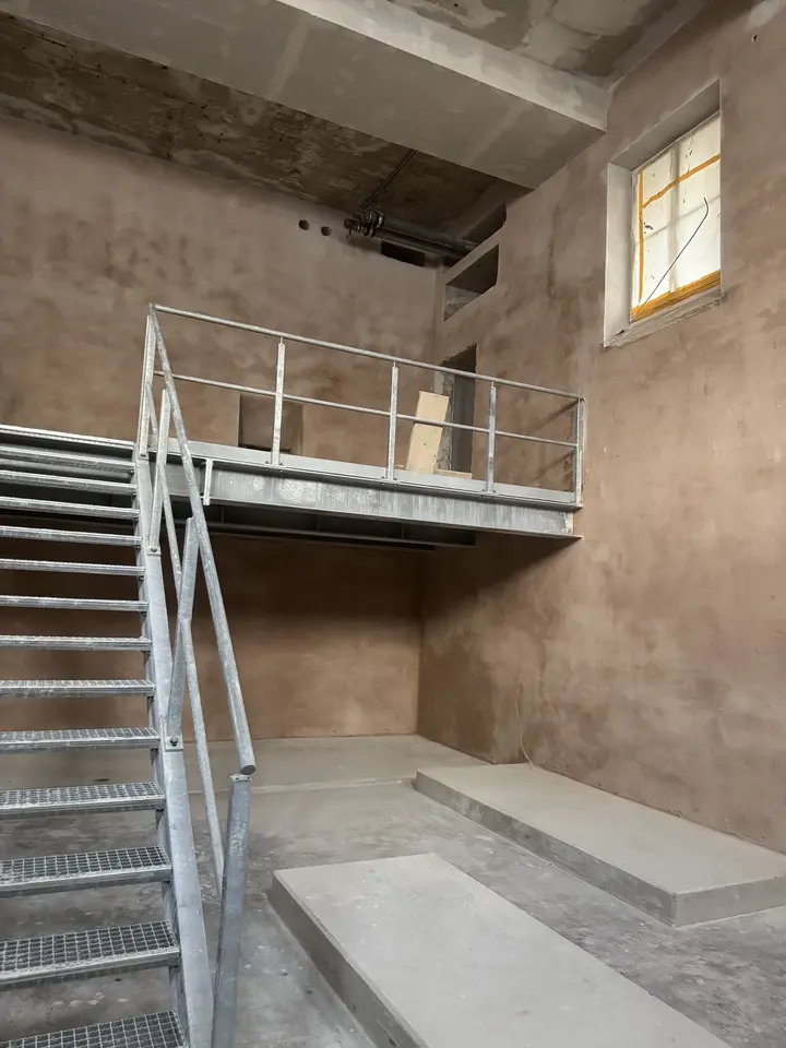 Entkernte Halle im Bestand mit neuer Stahltreppe zur Galerieebene vor unverputzten Wänden