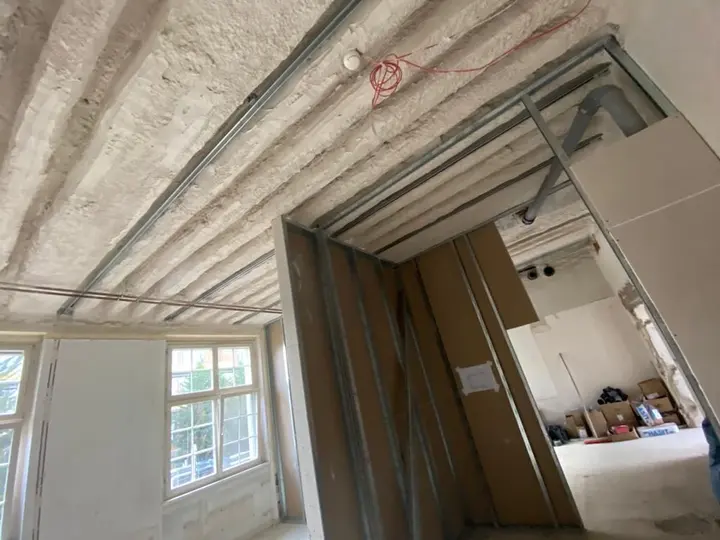 Metallständerwerk einer Trockenbau-Trennwand im Rohbau unter einer offenen Holzbalkendecke