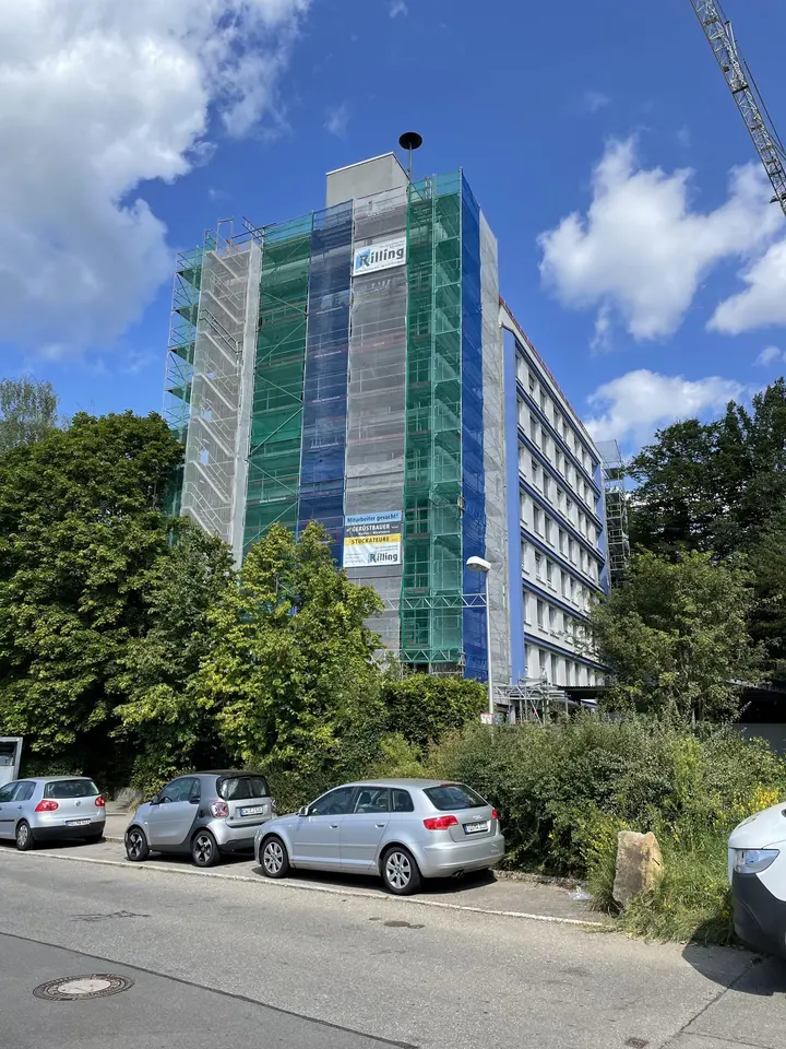 Bürohochhaus mit Fassadengerüst, grünem Schutznetz und Bauaufzug