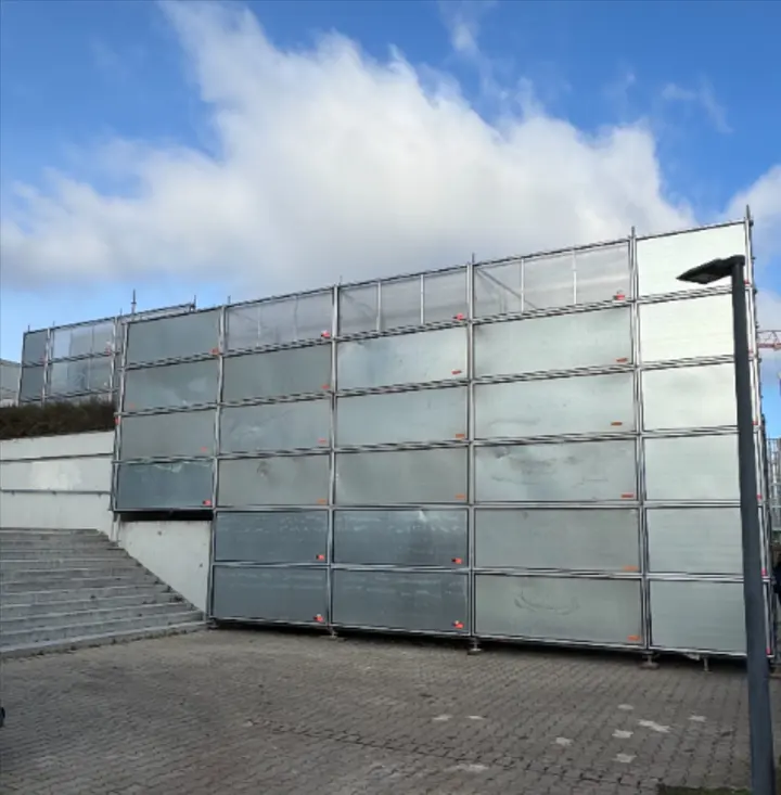 Freistehende Schutzwand aus Gerüstbauteilen mit Planenverkleidung auf einem Vorplatz