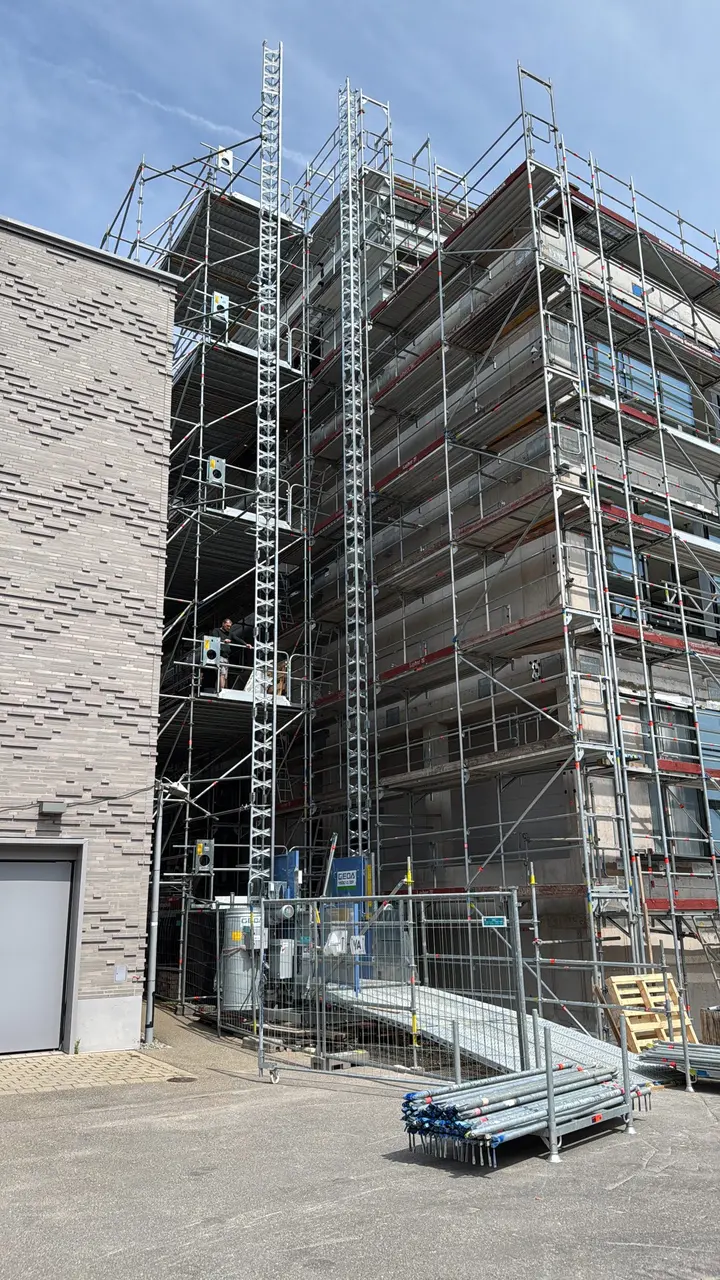 Fassadengerüst mit Materialaufzug, im Vordergrund gestapelte Gerüstbauteile