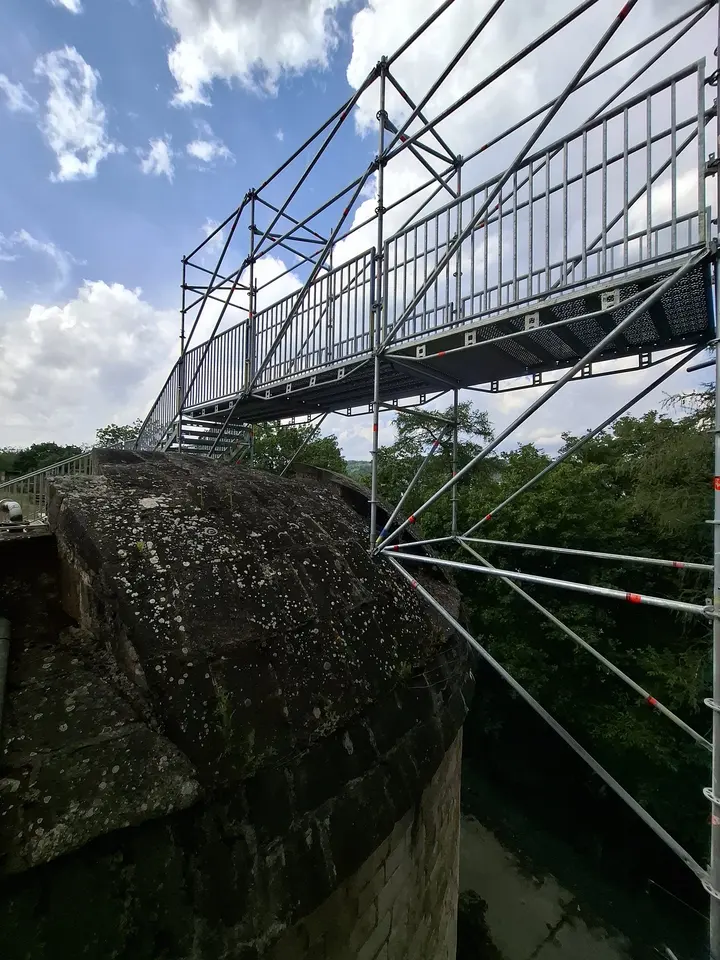 Auskragende Gerüstkonstruktion über einem Burggraben entlang einer historischen Mauer