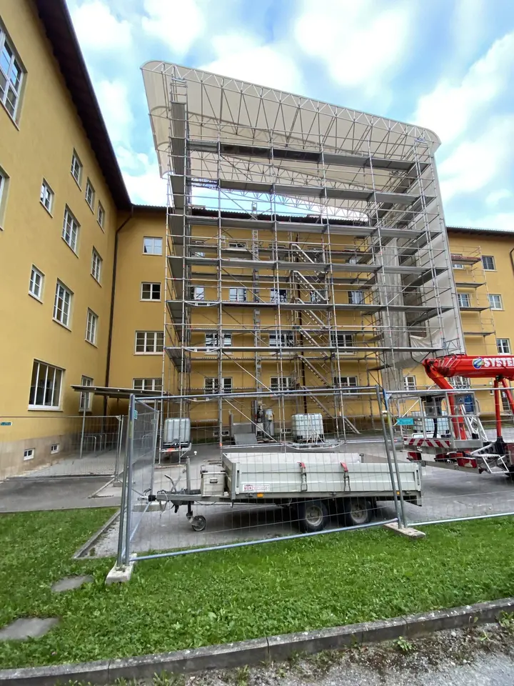 Fassadengerüst mit aufgesetztem Wetterschutzdach an einem gelb verputzten Altbau